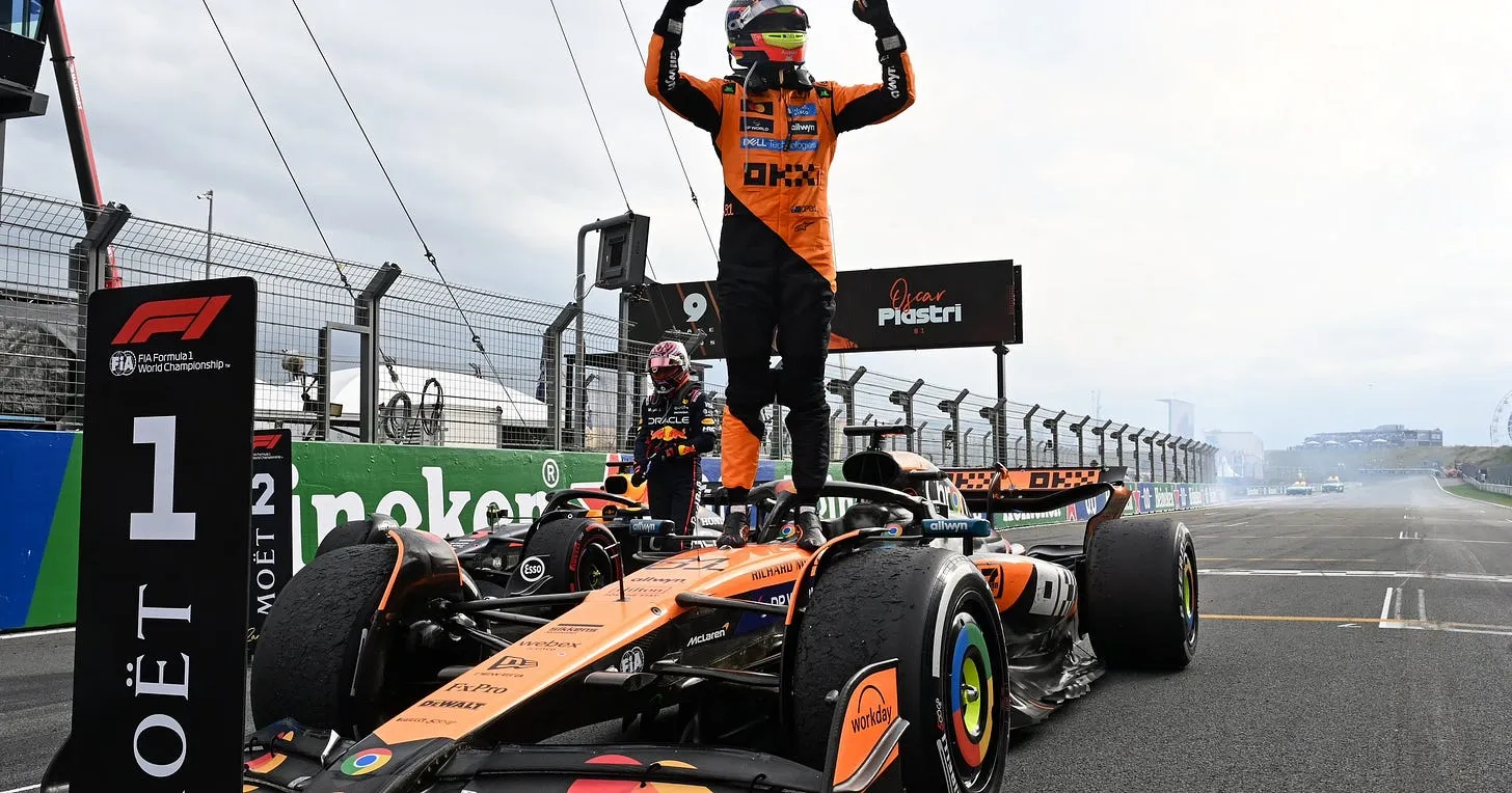 Oscar Piastri standing on his McLaren with both arms raised, celebrating after a race